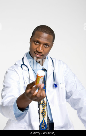 Ein freundlicher junger Arzt bietet dem Patienten einen Topf mit Pillen und trägt einen weißen Kittel und Stethoskop. Stockfoto