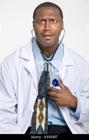 Humorvolle Foto eines Arztes hören auf sein eigenes Herz mit einem Stethoskop machen ein lustiges Gesicht und trägt einen weißen Mantel Stockfoto