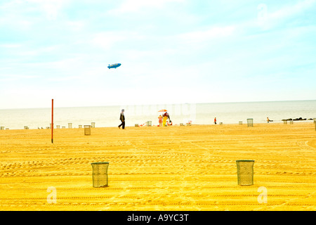 Landschaftlich malerisch beachscape von Mann zu Fuß auf Coney Island Strand mit ablimp flying Overhead in Brooklyn NY an einem sonnigen Tag Stockfoto