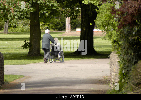 Alter Mann schieben alte Frau im Rollstuhl durch den park Stockfoto