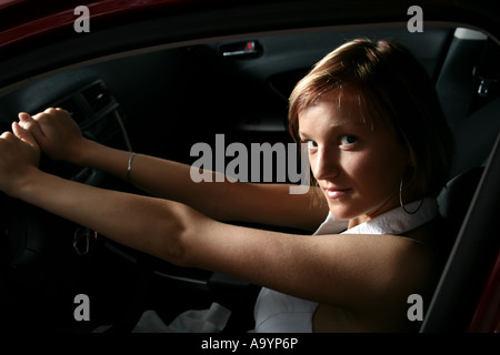 Junge Frau, die selbstbewusst in einem Auto sitzt, das Lenkrad mit einem subtilen Lächeln hält und Unabhängigkeit und einen modernen Lebensstil zum Ausdruck bringt. Stockfoto