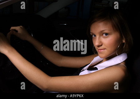 Junge Frau, die selbstbewusst in einem Auto sitzt, das Lenkrad mit einem subtilen Lächeln hält und Unabhängigkeit und einen modernen Lebensstil zum Ausdruck bringt. Stockfoto