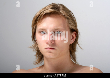 Ernsthafter junger Mann mit hellem Haar, der in einem Nahaufnahme-Porträt vor einem neutralen Hintergrund vor der Kamera steht und raue Emotionen und natürliche Eigenschaften hervorhebt Stockfoto