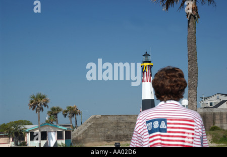 Eine Frau, die ein Hemd mit amerikanischer Flagge trägt, bewundert den berühmten Leuchtturm von Tybee Island in Savannah, Georgia, USA. Stockfoto