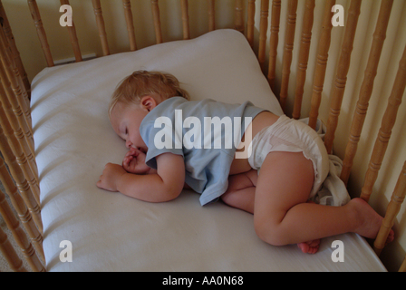 Baby schläft in einem Kinderbett nur mit einer Windel und blauen Top Stockfoto