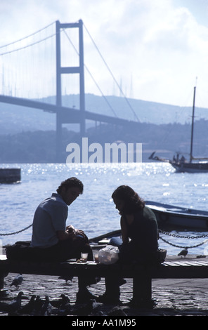 ISTANBUL. Ein junges Paar Essen ein Picknick-Mittagessen durch den Bosporus in Ortaköy, mit der ersten Bosporusbrücke hinter. 2006. Stockfoto