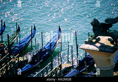 Italien, Venedig, steinerne Statue des geflügelten Löwen über blaue Gondeln auf dem Wasser Stockfoto