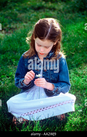 Ein kleines Mädchen sitzt mit einer Daisy Blume Stockfoto