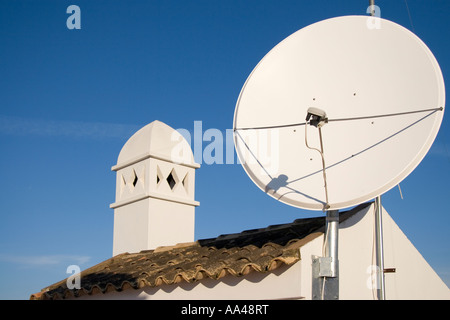 Eine Satellitenschüssel montiert durch das Dach eines traditionellen spanischen Gebäude mit einem maurischen Stil Kamin vor einem strahlend blauen Himmel Stockfoto