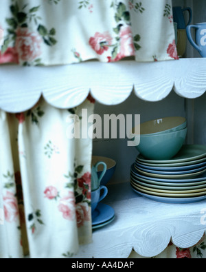 Nahaufnahme von floral Gardinen und überbackene Trim auf Regalen mit Pastell Geschirr Stockfoto