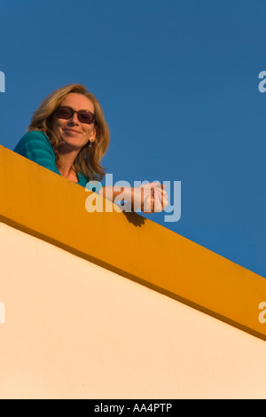 Frau mit langen Haaren tragen Sonnenbrillen 35 40 Jahre stützte sich auf einem Balkon in der warmen Abendsonne Stockfoto