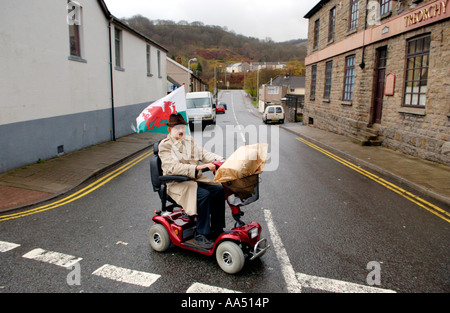 Älterer Mann auf Mobilität Roller roter Drache Flagge während Sie einkaufen auf der Straße in Treorchy Rhondda Valley South Wales UK Stockfoto