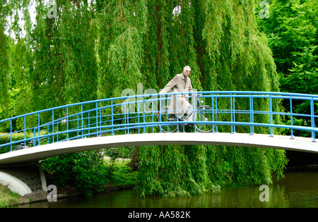 Ein älterer Mann auf einem Fahrrad über eine Brücke in den Vondelpark, Amsterdam angehalten, seine Balance zu erhalten. Stockfoto