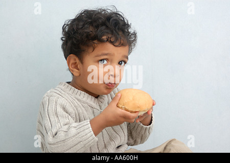 Kleine Indianerjunge von zweieinhalb Jahren frech und Lächeln auf den Lippen tragen weiße Pullover Käsebrot Essen Stockfoto