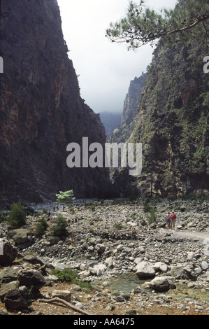 Kleine Gruppen von Menschen wandern entlang eines getrockneten Flussbettes im Sonnenlicht in Richtung der Eisernen Pforte der Samaria Schlucht, Kreta Stockfoto