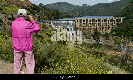 Ältere Frauen beobachten mit einem Fernglas, wie Wasser über den Wasserweg in den San Dieguito River am Lake Hodges Dam in Escondido, Kalifornien, USA, ausläuft Stockfoto