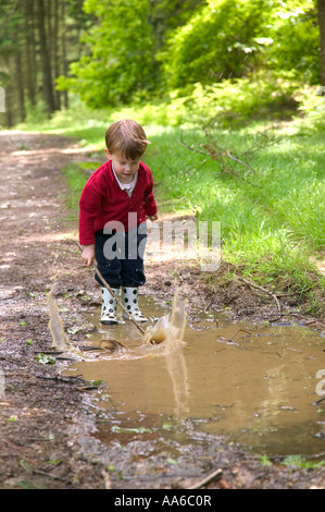 Kleinkind Spritzen in einer schlammigen Pfütze mit seinem Stock Stockfoto