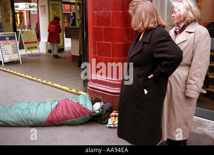 Obdachloser im Schlafsack liegend über Oxford Street in London als Käufer vorbei. Stockfoto