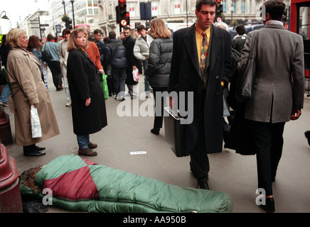 Obdachloser im Schlafsack liegend über Oxford Street in London als Käufer vorbei. Stockfoto