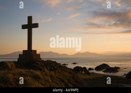 Steinkreuz in der Silhouette bei Sonnenuntergang am felsigen Tipp von Llanddwyn Island Newborough Isle of Anglesey North Wales UK Großbritannien Stockfoto