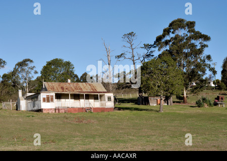 Landhaus Towamba New South Wales | TOWAMBA, New South Wales, Australien – Ein Weatherboard-Farmhaus mit einem verrosteten Wellblechdach und einer umlaufenden Veranda steht inmitten von grasenden Paddocks in der Nähe von Towamba, im Hinterland der Südküste von New South Wales. Ziegelsteine und verstreute Nebengebäude aus Holz kennzeichnen es als ein bewirtschaftetes ländliches Anwesen, typisch für die Bauernarchitektur des Viertels Ende des 19. Und Anfang des 20. Jahrhunderts. Stockfoto