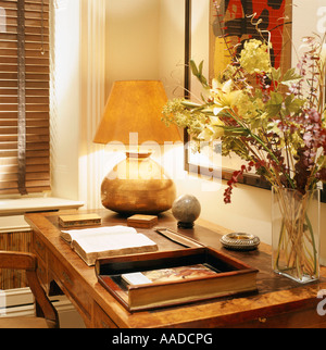 Gold beleuchtete Lampe und Blumenarrangement auf Schreibtisch mit Buch öffnen Stockfoto