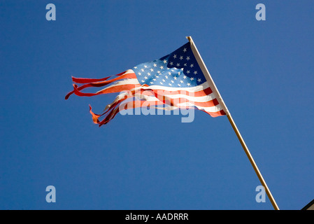 Alt und zerrissen durch Wind, die amerikanische Flagge am Mast über Gebäude fliegt Stockfoto