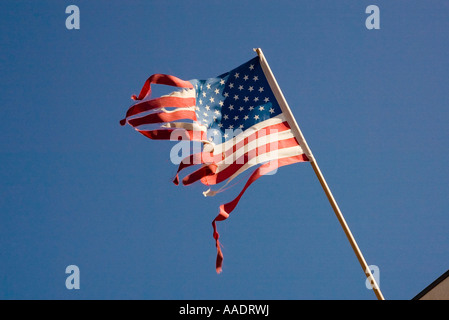 Alt und zerrissen durch Wind, die amerikanische Flagge am Mast über Gebäude fliegt Stockfoto