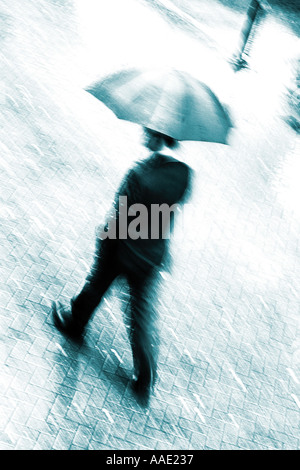 Ein Geschäftsmann im Anzug zu Fuß, mit Geschwindigkeit unter einen Regenschirm im Regen mit Bewegungsunschärfe, Chester, Cheshire, UK Stockfoto