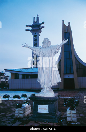 Post Moderne Saint Bonaventura römisch-katholische Kathedrale Banja Luka durch Dämmerung und Statue von Jesus Christus mit Armen öffnen in Empfang Stockfoto