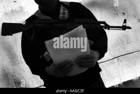 Ein Terrorist, der in einer Sturmhaube gekleidet ist und ein Kalaschnikow-Gewehr AK47 hält und einen Gürtel aus Kugeln neben einem Land rover trägt, der vom Modell aus aufgestellt wird Stockfoto