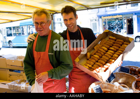 Zwei besuchen Männer Markt männliche französische Händler verkaufen bretonische Kekse auf den Stall in Aberystwyth Ceredigion Wales Stockfoto