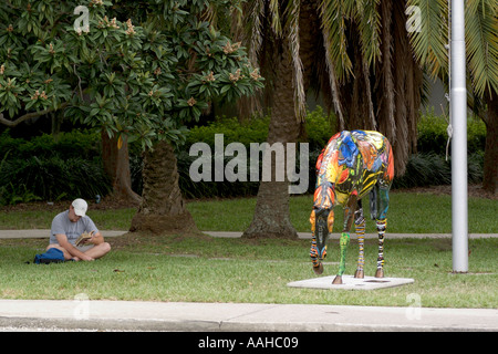 Schüler lesen ruhig sitzend auf grüner Wiese in der Nähe der bunt bemalten Skulptur eines Pferdes Stockfoto