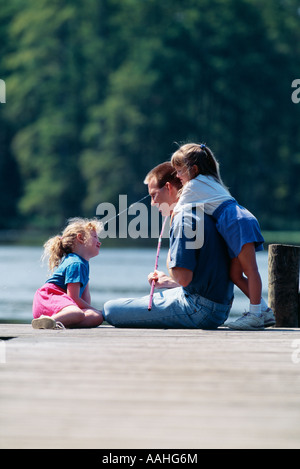 Vater sitzt mit Töchtern auf Pier See Stockfoto