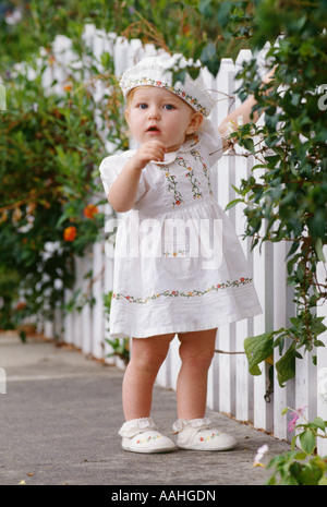 Babymädchen stehen von weißen Lattenzaun in liebenswert Kleid und Hut Stockfoto