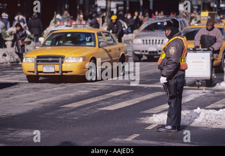 Gelbes Taxi neben macys mit einem diensthabenden Polizisten, der in warmer Winterkleidung mit den Schneerüsten auf dem Boden in New York City, USA, gekleidet ist Stockfoto