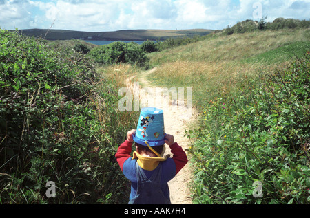 Ein kleiner Junge trägt einen Eimer auf dem Kopf, während zu Fuß entlang einer Küste, Rock, Cornwall, UK. Stockfoto