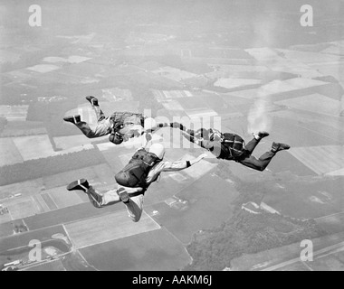 1970ER JAHREN DREI MÄNNER HALTEN HÄNDE FALLSCHIRMSPRINGEN Stockfoto
