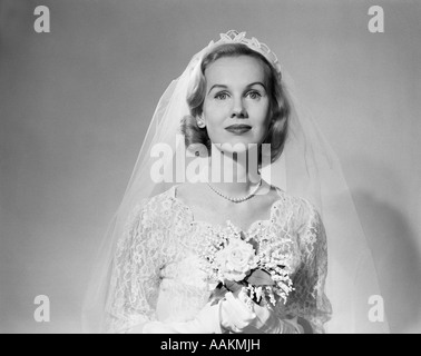 1950ER JAHRE PORTRAIT FRAU BRAUT TRAGEN WEIßE HOCHZEIT KLEID SCHLEIER PERLENSCHNUR HÄLT EINEN BLUMENSTRAUß BLICK IN DIE KAMERA Stockfoto