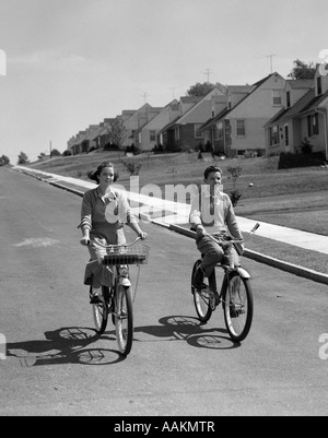 1950ER JAHRE TEEN BOY GIRL RIDING BIKES VORORT NACHBARSCHAFT STRAßE Stockfoto