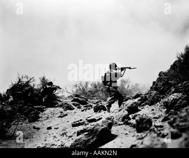 1940ER JAHRE BEKÄMPFUNG DER US ARMY INFANTERIE MÄNNER SCHIEßEN GEWEHRE IN AKTION MIT SCHWEREN RUCKSÄCKEN WÄHREND DES 2. WELTKRIEGES Stockfoto
