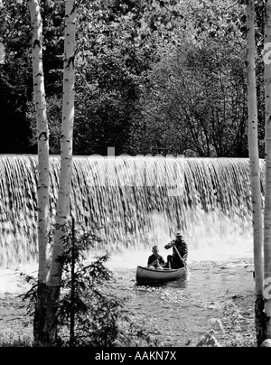 1970ER JAHREN VATER & SOHN IM KANU VOR DER WASSERFALL MIT VATER RUDERN & SOHN ANGELN Stockfoto