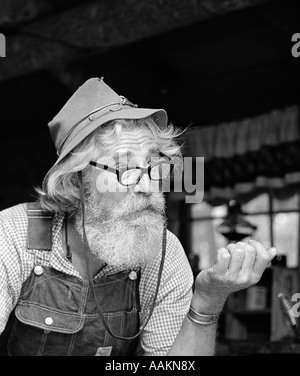 1970ER JAHRE ÄLTEREN MANN BERG HANDWERKER CHARAKTER FILZHUT OVERALLS KARIERTE BAUMWOLLHEMD MIT BRILLE TRAGEN BART IM FREIEN Stockfoto