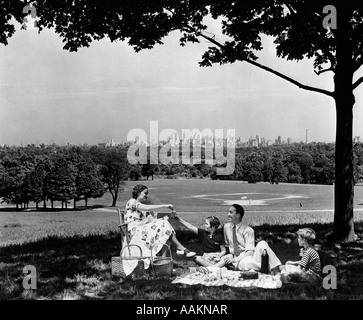 1930S 1940S FAMILIE PICKNICK UNTER EINEM BAUM IM FAIRMONT PARK MIT SKYLINE VON PHILADELPHIA PA WEITER HORIZONT Stockfoto