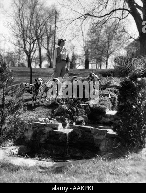 1930ER JAHREN FRAU ZU FUß 4 HUNDE DALMATINER AN LEINE AM GELÄNDE GARTEN DES HAUS LANDGUT Stockfoto