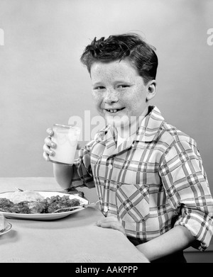 1930S 1940S LÄCHELND FRECKLE DREINBLICKENDEN JUNGEN SITZEN ESSTISCH HOLDING GLAS MILCH Stockfoto