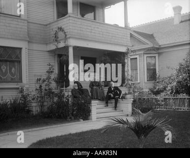 1890S 1900S SENIOR MÄNNER UND FRAUEN SITZEN AUF FRONT PORCH AUßEN HAUS Stockfoto