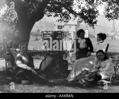 1900S 1890S REIFE FRAUEN UND JUGENDLICHEN MÄDCHEN SITZEN AUF GRASS AUßEN HOME Stockfoto