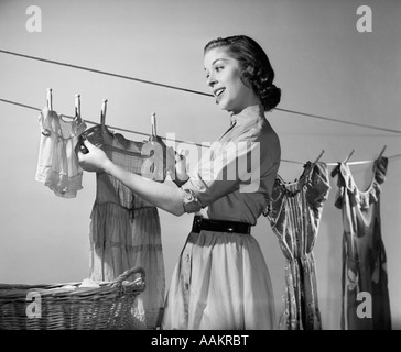 1950ER JAHREN LÄCHELNDE FRAU HAUSFRAU AUFHÄNGEN AUF DER WÄSCHELEINE ZUM TROCKNEN WASCHEN Stockfoto