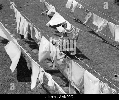 1950ER JAHREN FRAU HÄNGENDE WÄSCHE IM FREIEN AUF MEHREREN WÄSCHELEINEN Stockfoto